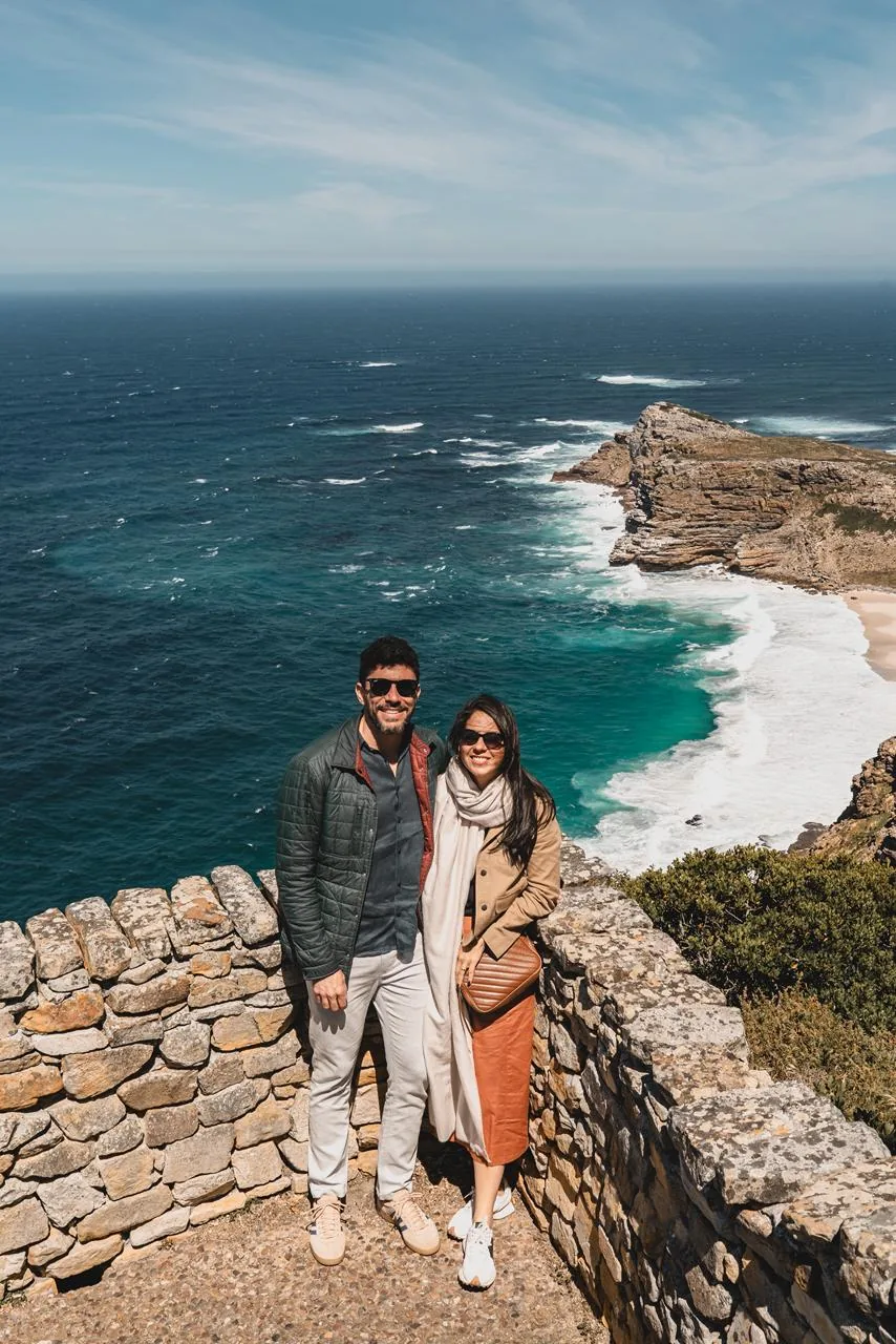Um casal permanece diante da costa enquanto a paisagem ocupa quase toda a fotografia.