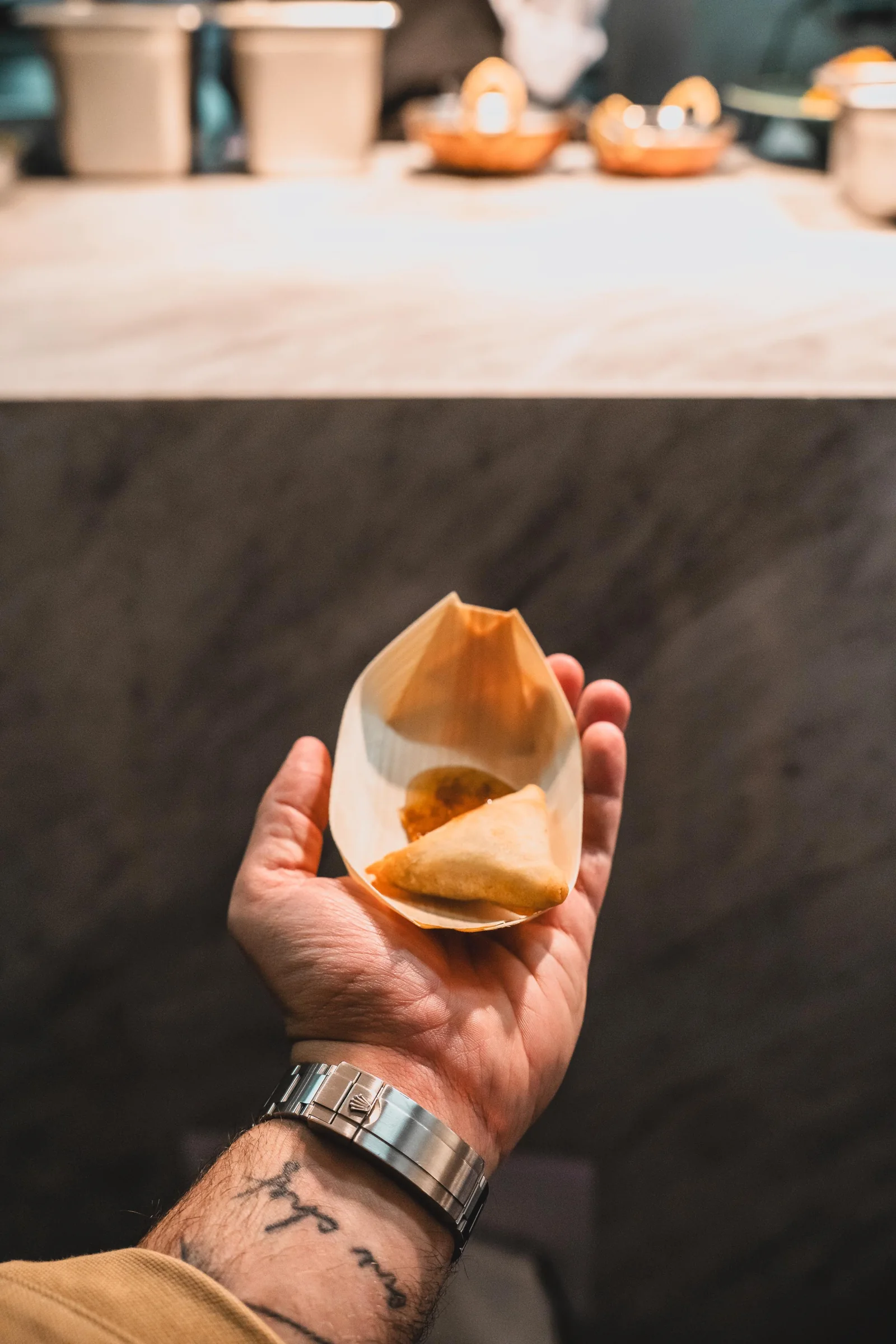 Uma mão segura uma samosa recém-preparada diante da bancada